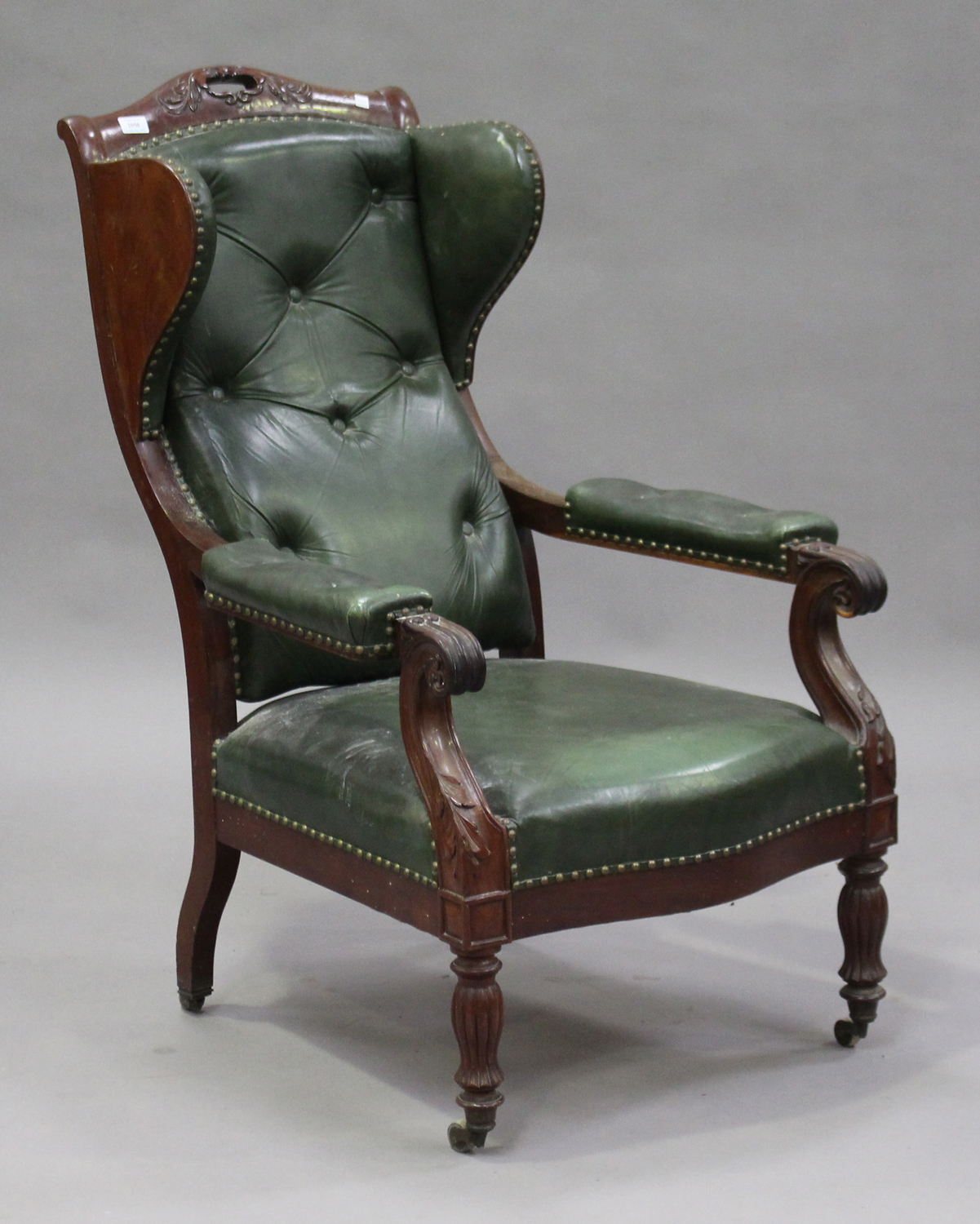 A 19th century French mahogany and buttoned green leather wing back armchair with carved foliate