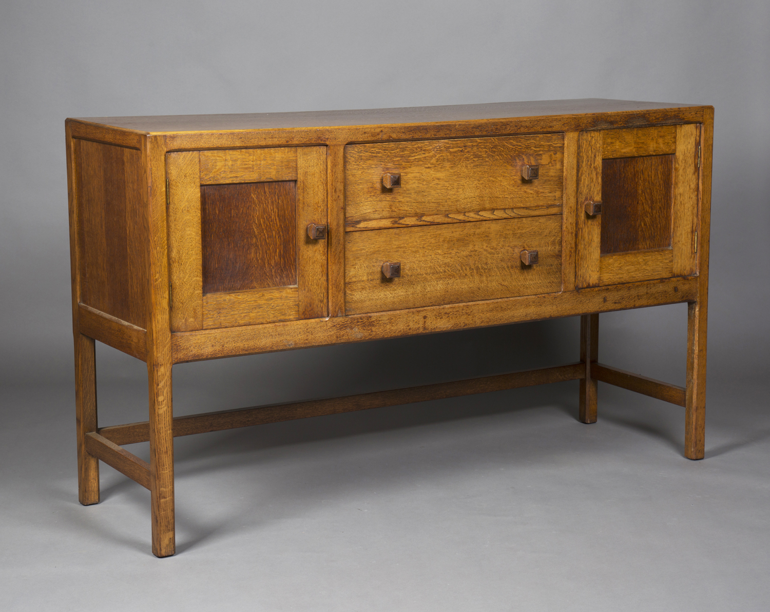 An early 20th century oak sideboard by Heals, the chamfered top above two drawers flanked by