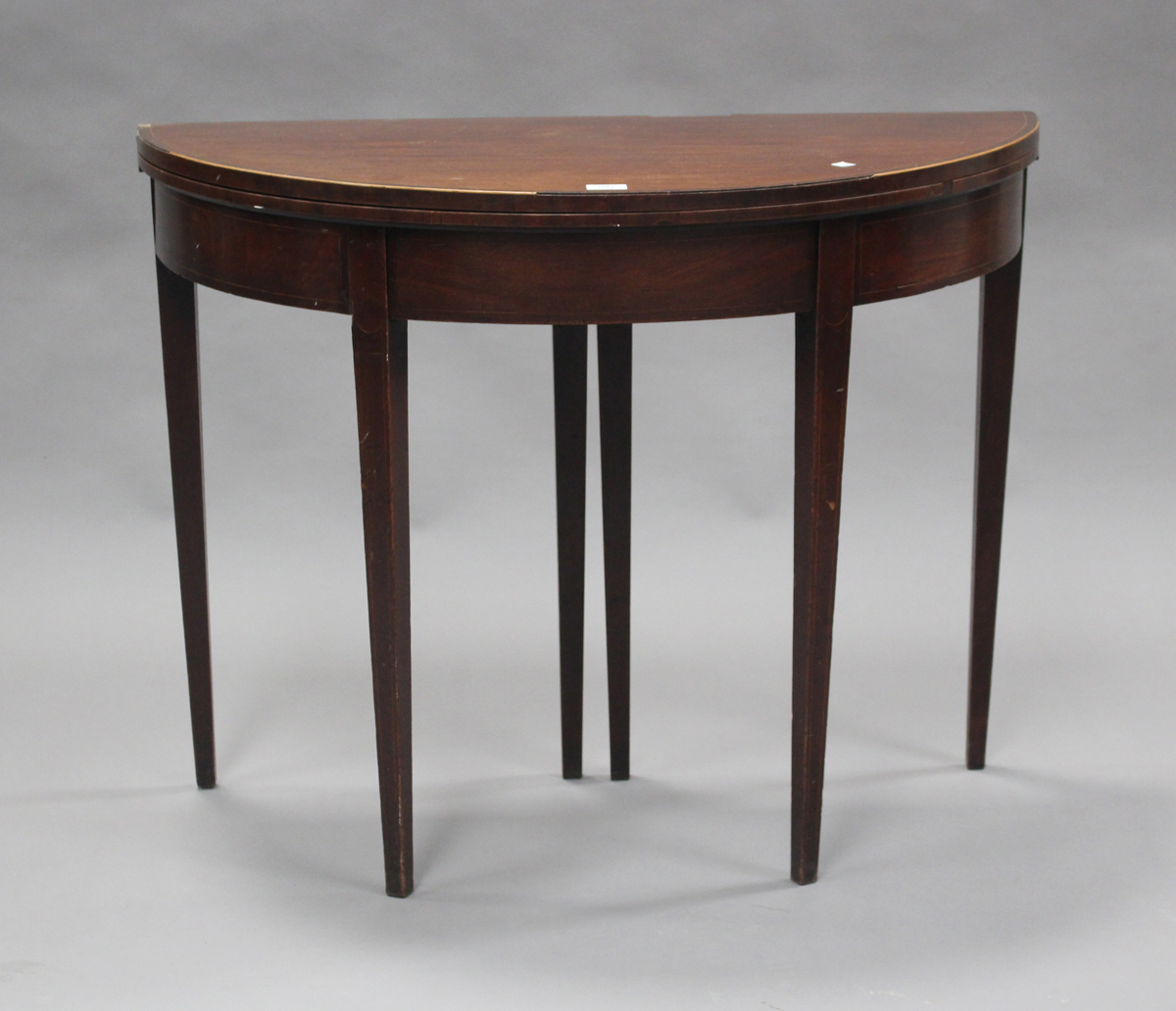 A late George III mahogany fold-over demi-lune tea table with crossbanded borders and boxwood