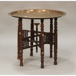 A late 19th/early 20th century Middle Eastern Islamic tray-top table, the circular copper tray