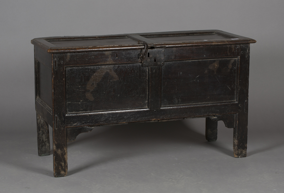 An early 18th century oak panelled coffer, the hinged lid with wrought iron latch, raised on long