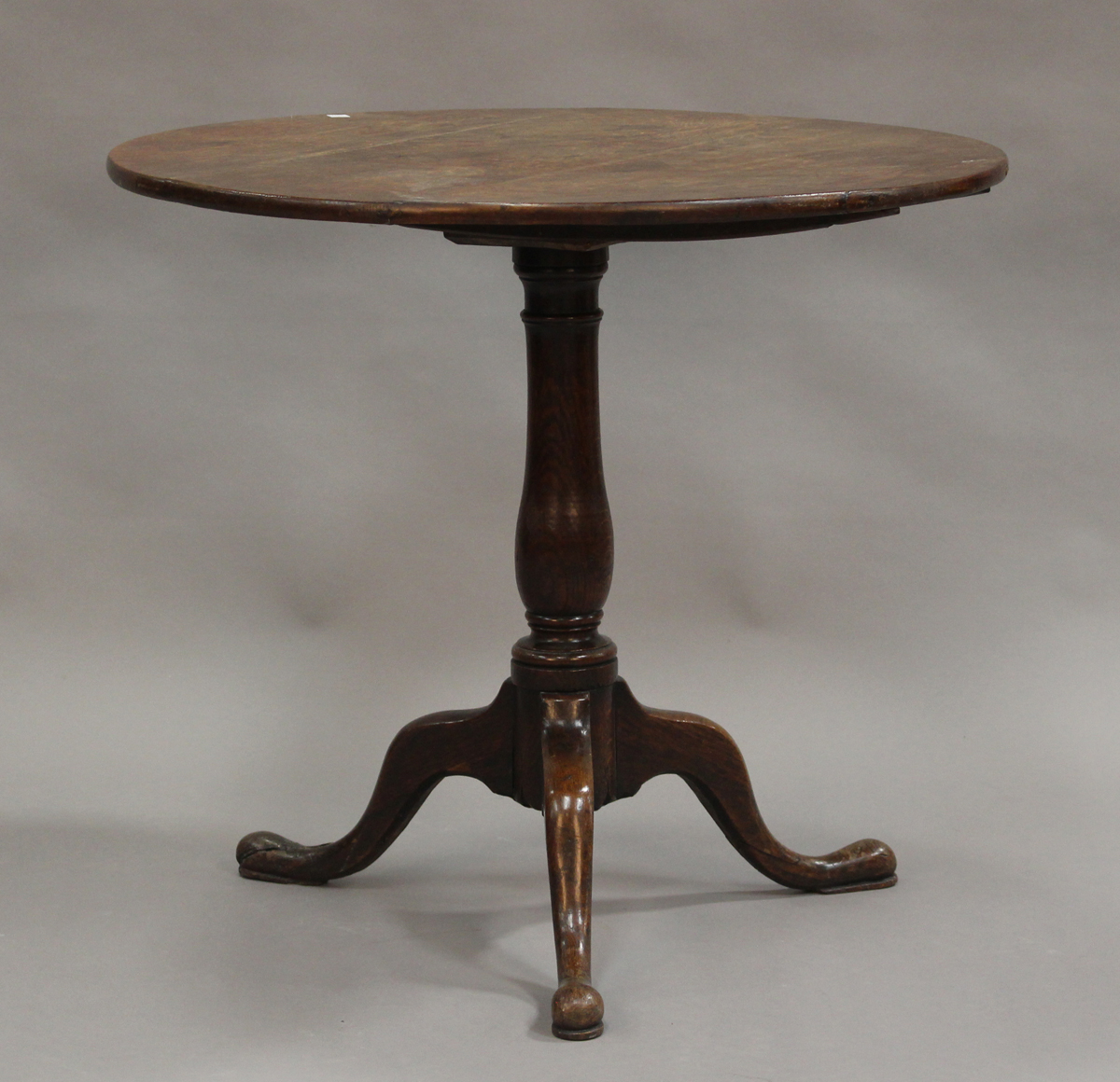 A late George III provincial oak circular tip-top wine table, raised on a turned baluster stem and
