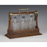 An Edwardian oak and nickel plate mounted three-bottle tantalus, fitted with three cut glass