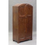 An early 20th century oak wardrobe, in the manner of Heals, the arched top above two panelled doors,