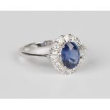 An 18ct white gold, sapphire and diamond cluster ring, claw set with an oval cut sapphire within a