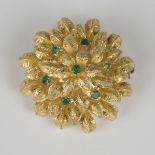 A gold and emerald brooch of shaped circular floral form, mounted with seven circular cut
