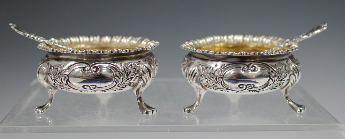 A pair of Edwardian silver circular salts with gadrooned rims and chased floral decoration, on