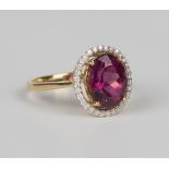 An 18ct gold ring, claw set with an oval cut shimoyo rubellite within a surround of thirty-two