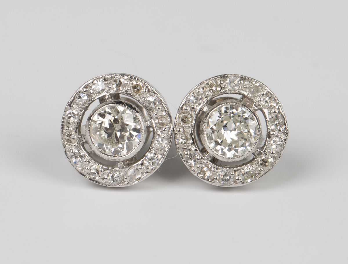 A pair of white gold and diamond earstuds, each collet set with the principal circular cut diamond