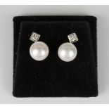 A pair of white gold and cultured pearl earrings, each mounted with a circular cut diamond within