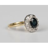 A gold, sapphire and diamond oval cluster ring, claw set with the oval cut sapphire within a