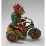 A German tinplate clockwork monkey, wearing a Fez, jacket and trousers, riding on a tricycle, length