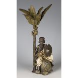 A 20th century cold painted cast bronze figure of a young man, seated on a rock below a palm tree,