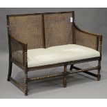 A George V oak framed bergère settee, the slightly double-bowed back and sides with caned panels, on