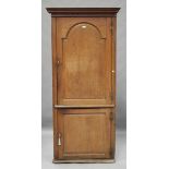 A George III oak floor standing corner cabinet, the arched panel door enclosing shaped shelves,