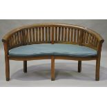 A modern teak banana garden bench of curved form, fitted with a cushion, height 84cm, width 159cm,