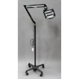 A mid-20th century black finished ophthalmic examination lamp by Burton, raised on a wheeled base,