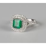 An 18ct white gold, emerald and diamond cluster ring, claw set with a square cut emerald within an