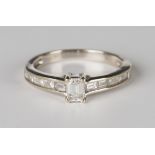 A white gold and diamond ring, claw set with the principal cut cornered rectangular emerald cut