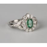 A platinum, emerald and diamond ring, collet set with an oval cut emerald within a surround of