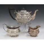 An Edwardian silver three-piece tea set, each piece of half-reeded cushion form with gadrooned and