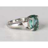 A platinum, emerald and diamond ring, claw set with an oval cut emerald between rectangular cut
