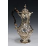 A late Victorian silver hot water jug of baluster form with domed hinged lid and finial, decorated