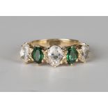 A gold ring, mounted with two oval cut green gems alternating with three larger oval cut