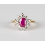An 18ct gold, ruby and diamond cluster ring, claw set with an oval cut ruby within a surround of