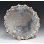 A large late Victorian silver salver with cast scroll and scalloped rim, raised on four volute