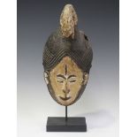 An African carved and painted wooden mask, Igbo tribe, Nigeria, modelled with a wild cat