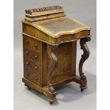 A late Victorian walnut Davenport, the serpentine fronted writing slope raised on carved cabriole
