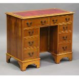 A late 20th century reproduction yew kneehole desk, the top inset with gilt-tooled red leather,