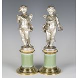 A pair of late 19th century silvered spelter models of cherubs, standing on associated brass mounted