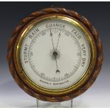 An Edwardian oak framed aneroid barometer with printed ceramic dial within a carved ropetwist