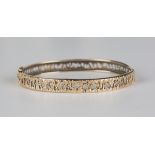 A 9ct gold oval hinged bangle with pierced bark textured decoration, on a snap clasp, inside width