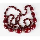 A single row necklace of graduated oval reconstituted cherry coloured amber beads, length 94.5cm.