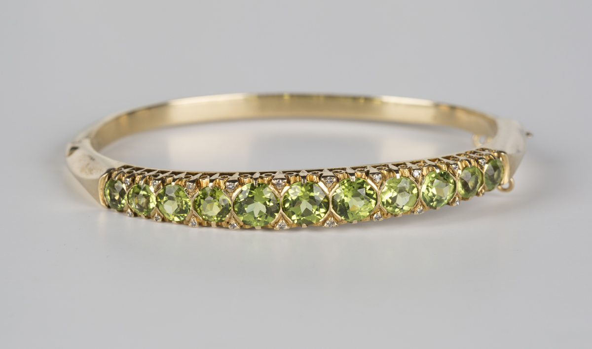 A 9ct gold, peridot and diamond oval hinged bangle, mounted with a row of eleven circular cut