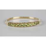 A 9ct gold, peridot and diamond oval hinged bangle, mounted with a row of eleven circular cut