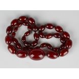A single row necklace of oval graduated reconstituted cherry coloured amber beads on a screw