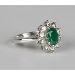 A white gold, emerald and diamond cluster ring, claw set with an oval cut emerald within a