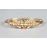 A gold, coral and seed pearl oval hinged bangle, circa 1910, the front in a pierced scrolling