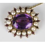 A gold, amethyst, half-pearl and red gem set brooch, mounted with an oval cut amethyst in a surround