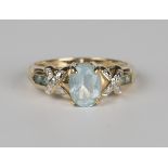 A 9ct gold ring, claw set with an oval cut blue topaz between diamond set 'X' shaped shoulders,