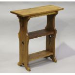 An Edwardian Arts and Crafts oak three-tier book table, the shaped sides pierced with stylized