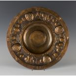 An early 20th century Arts and Crafts pressed copper charger, the border decorated in relief with