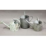 A group of five galvanized watering cans, another watering can, a galvanized two-handled tub and