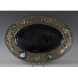 An early 20th century Arts and Crafts pewter mounted oval wall mirror, the frame worked with two