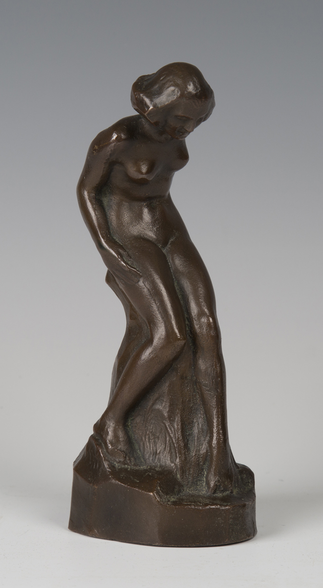 An early 20th century brown patinated cast bronze figure of a nude lady, leaning upon a rocky