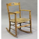 An early 20th century Arts and Crafts beech framed rocking armchair with a rush seat, height 80cm,